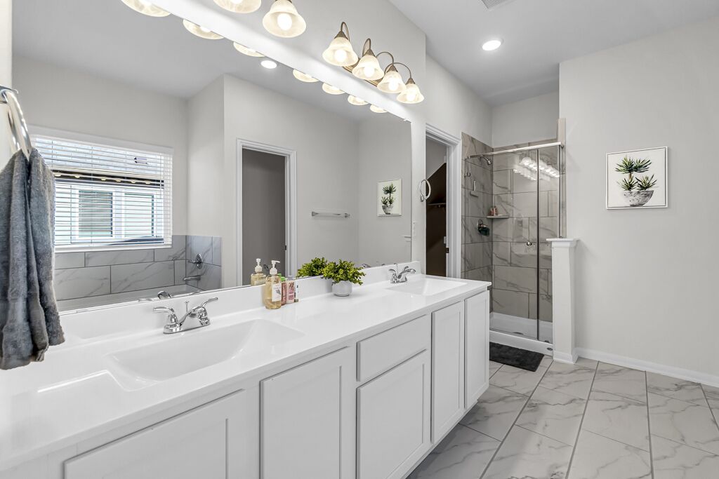 A modern bathroom with a large mirror, dual sinks, and a walk-in shower.