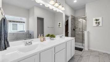 A modern bathroom with a large mirror, dual sinks, and a walk-in shower.