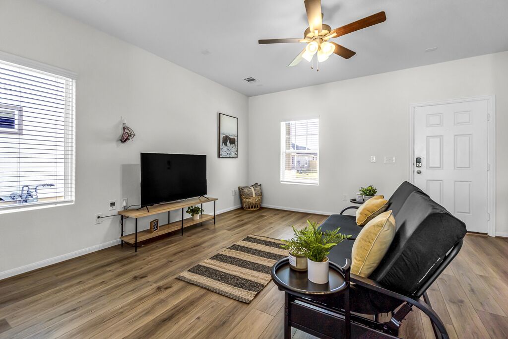 A spacious living room with a flat-screen TV, a ceiling fan, and a black leather sofa.