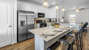 A modern kitchen with stainless steel appliances, a central island with bar stools, pendant lighting, and a ceiling fan. - Single Family Home 25 Minutes from Downtown  (Hutto)