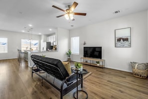 Un salon moderne avec un canapé noir, un téléviseur et un ventilateur de plafond.