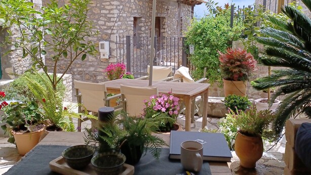 An outdoor patio with a table, chairs, and umbrellas. There are potted plants and a stone building in the background. - Beautiful cottage tastefully decorated close to amenities (Chrani)