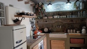 A rustic kitchen with a white refrigerator, wooden cabinets, a stone wall, and a hanging light fixture. - Beautiful cottage tastefully decorated close to amenities (Chrani)