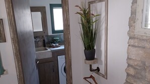 A narrow hallway with a stone floor leading to a kitchen area. A potted plant hangs on the wall, and a coat rack is visible. - Beautiful cottage tastefully decorated close to amenities (Chrani)