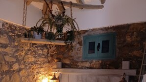 A rustic bedroom with a stone wall, wooden beams, a bed with patterned pillows, and hanging plants. - Beautiful cottage tastefully decorated close to amenities (Chrani)