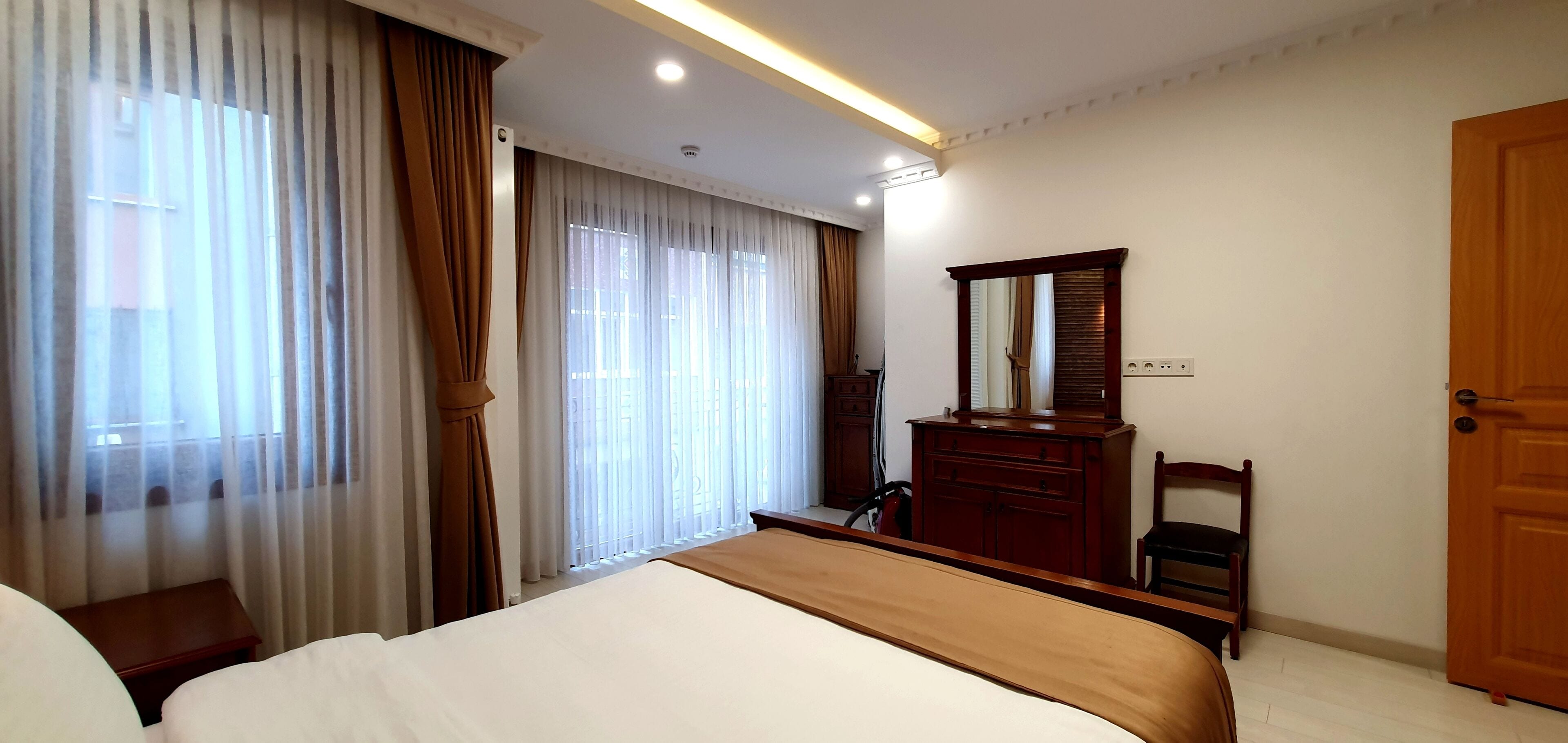 Une chambre d’hôtel avec un lit, une commode en bois, une chaise, un miroir et une porte.