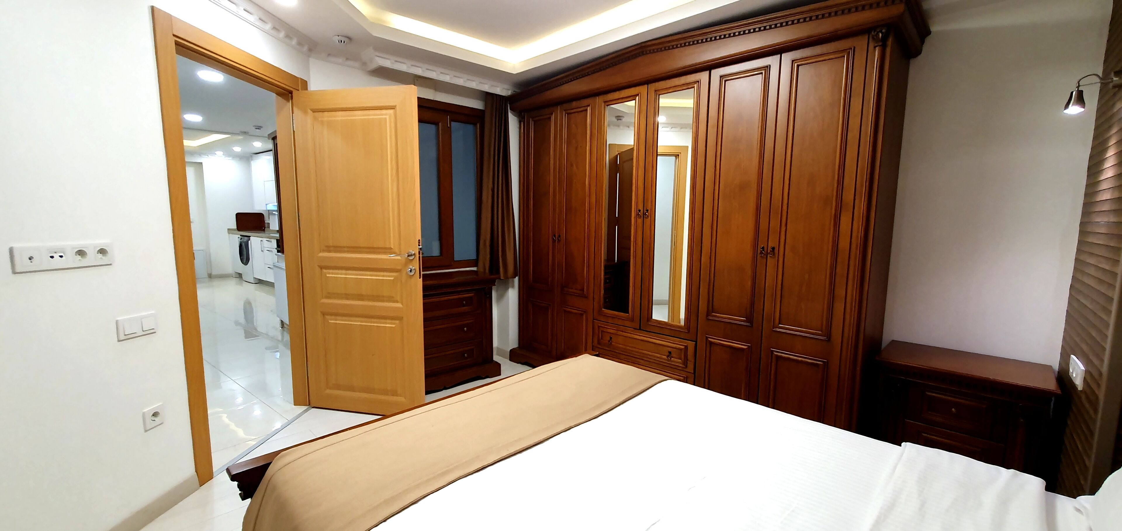 A bedroom with a bed, wooden wardrobe, and a mirror.