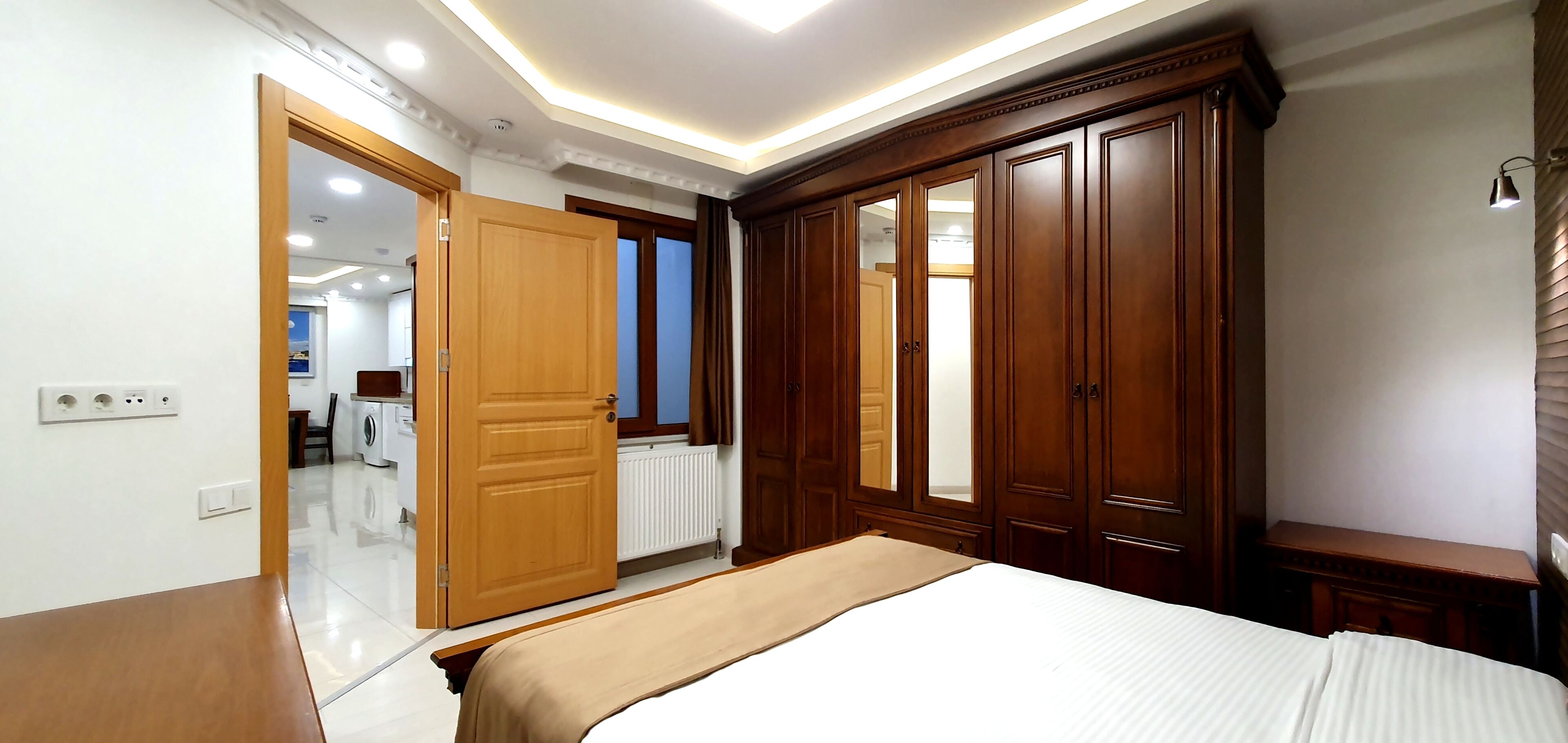 Ein Schlafzimmer mit einem großen Bett, einem Holzschrank und einem durchgehenden Türrahmen einsehbarer Badezimmer.