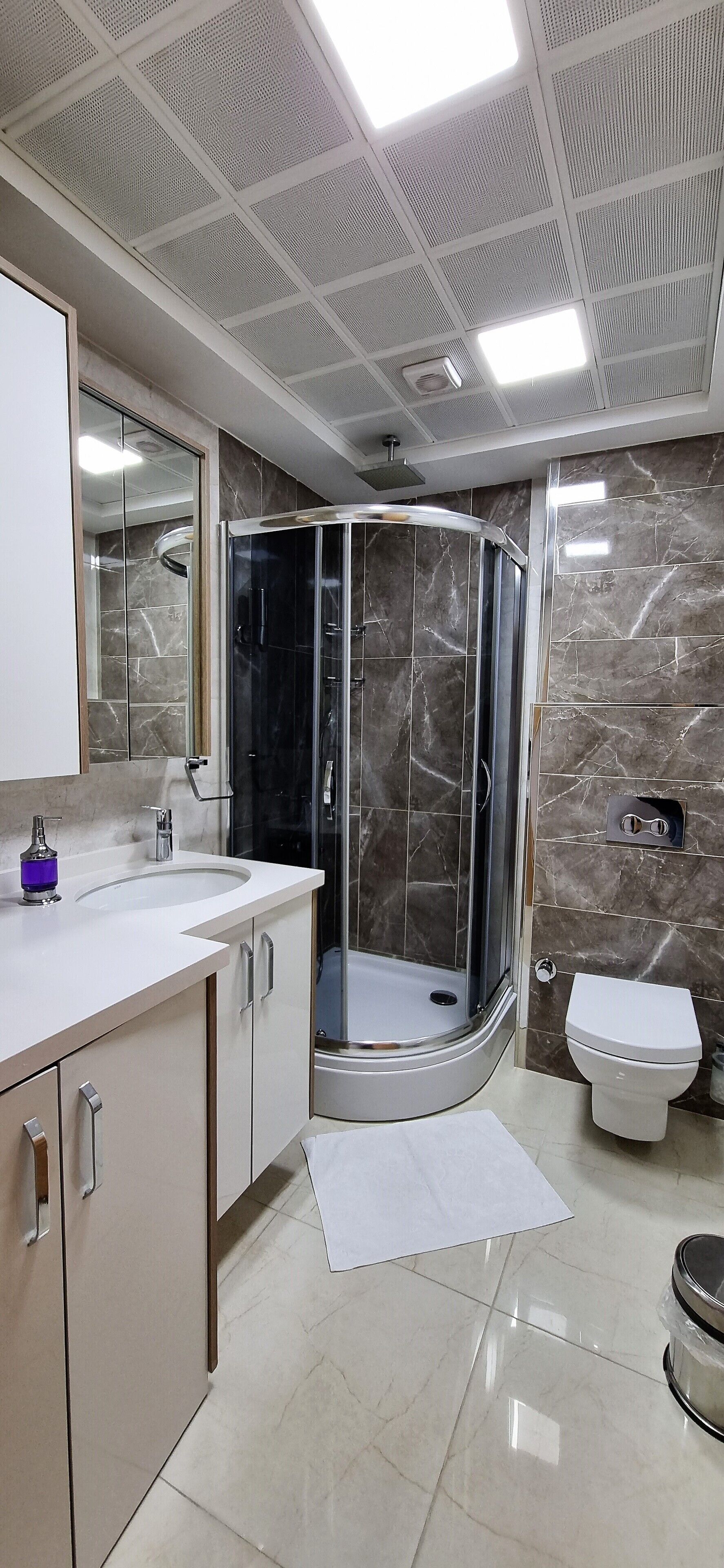 A modern bathroom with a curved glass shower enclosure, a white sink, and a toilet.