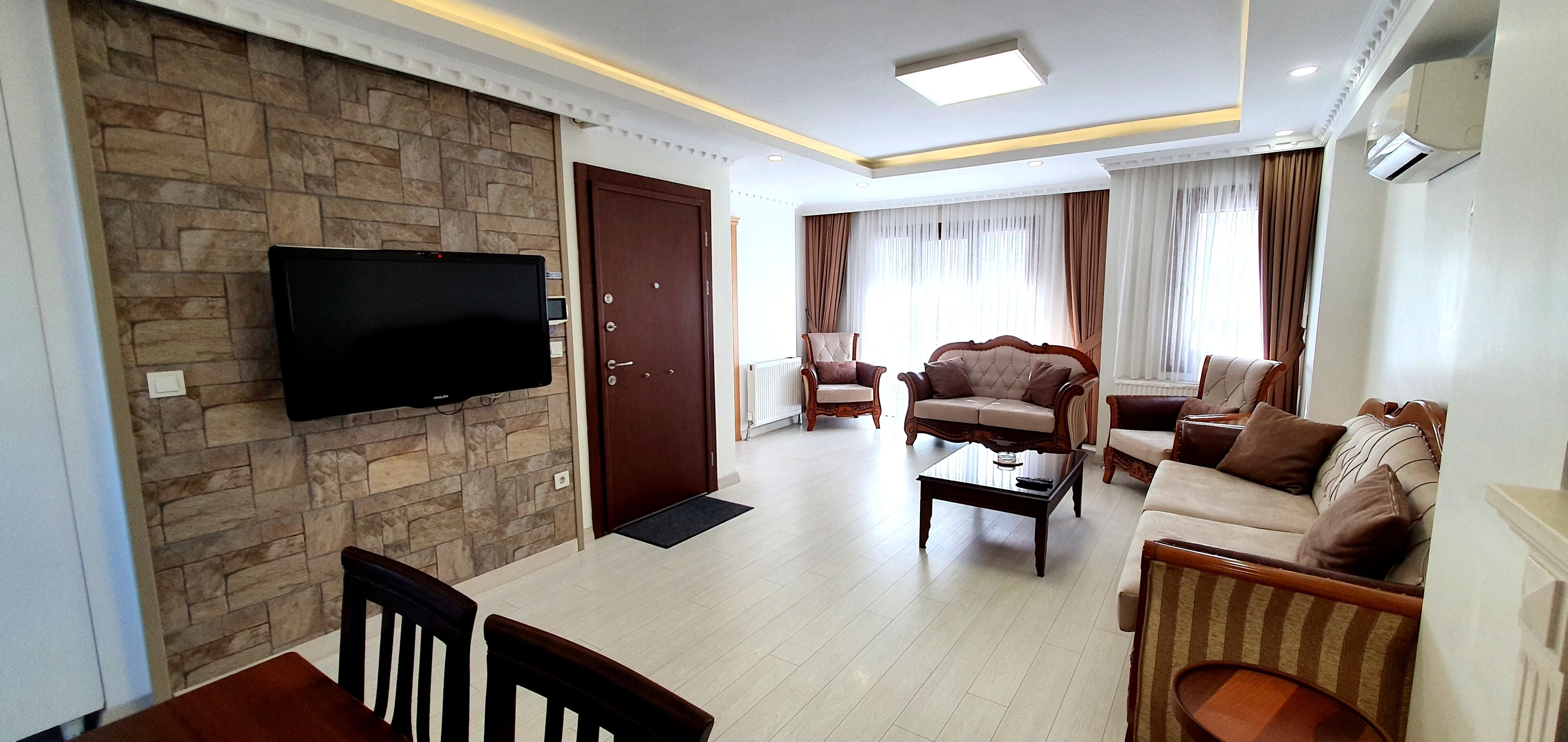 A living room with a stone wall, a flat-screen TV, a wooden dining table, and a sofa.