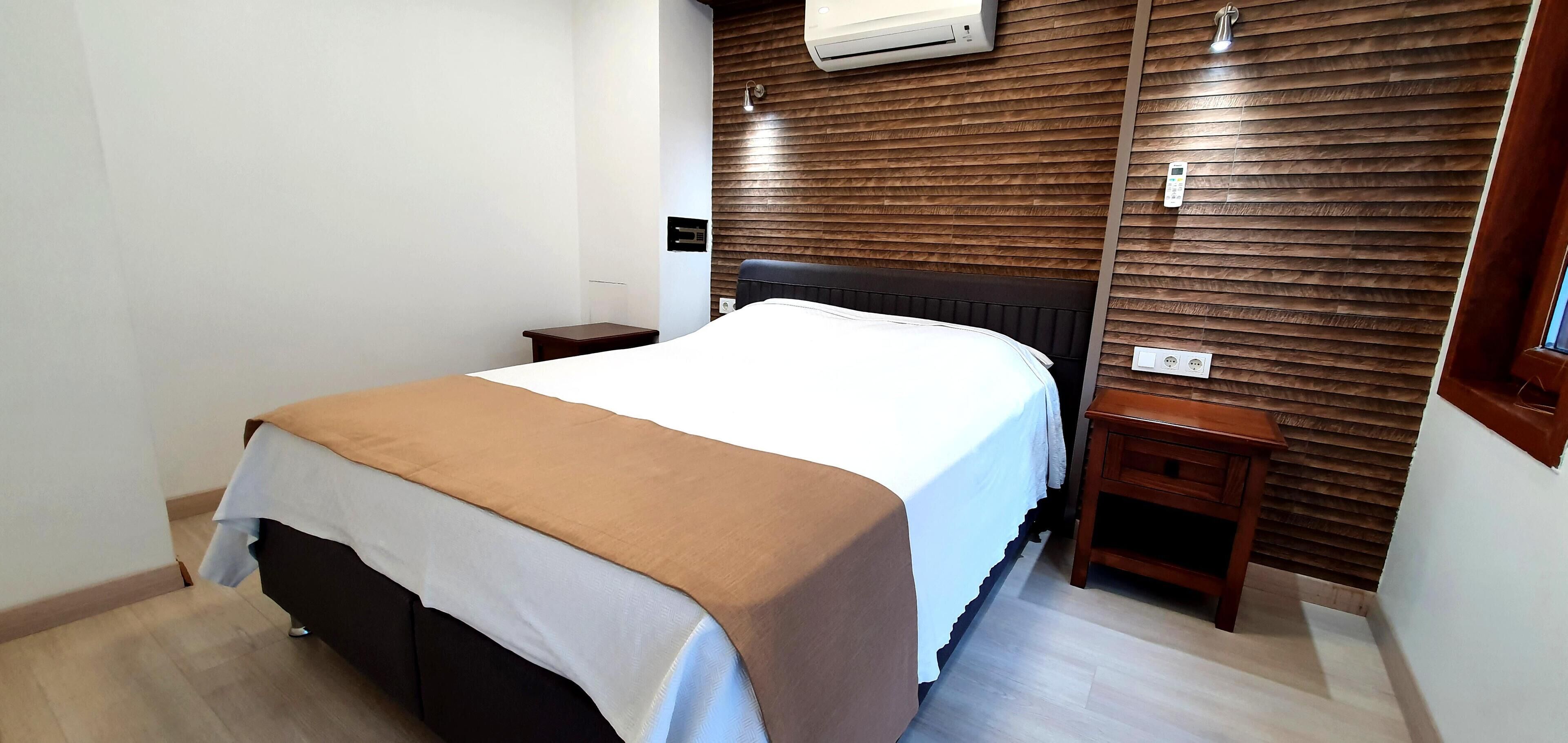 Habitación de hotel con cama, mesitas de noche, panel de pared de madera, unidad de aire acondicionado y ventana.