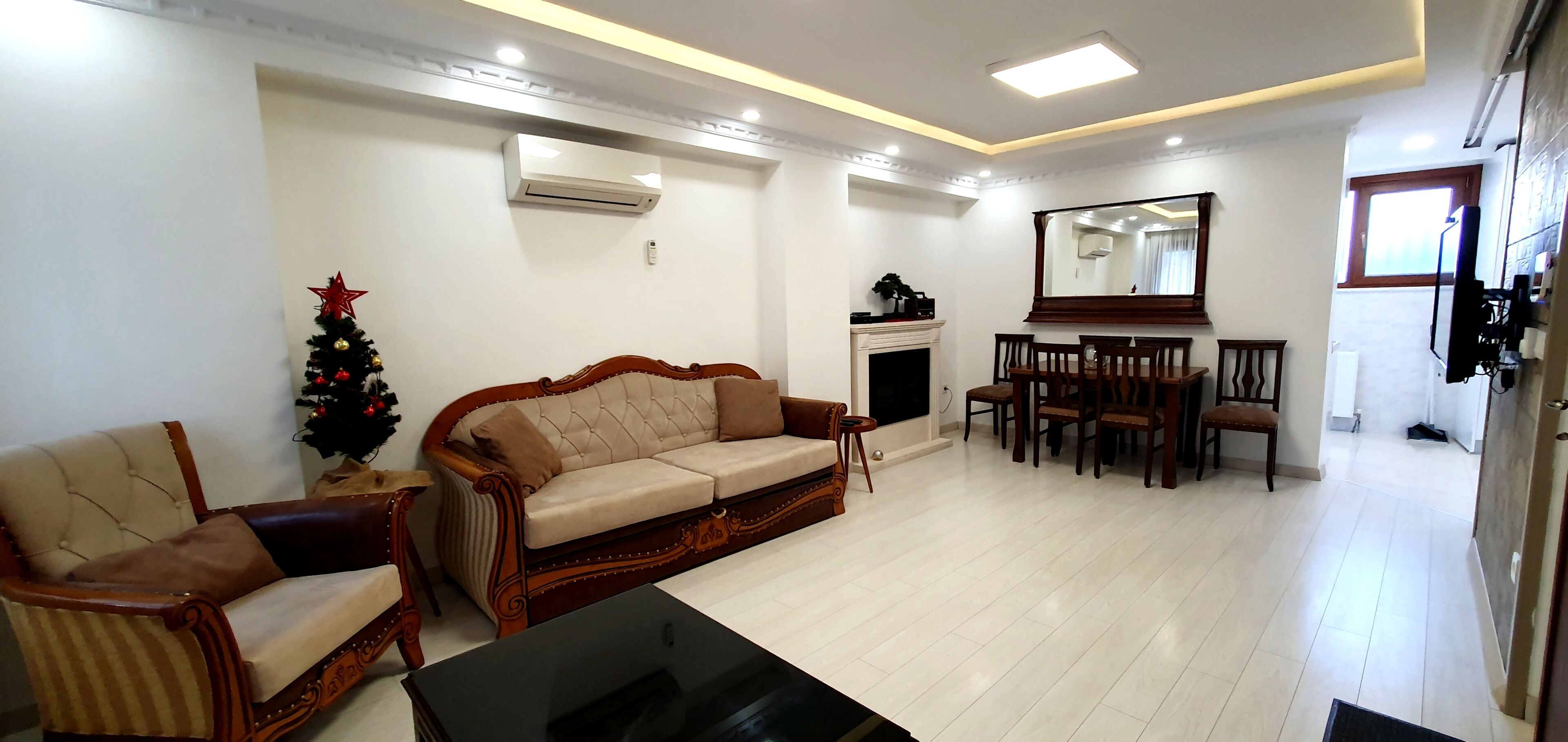 A living room with a sofa, armchair, dining table, chairs, a fireplace, and a Christmas tree.