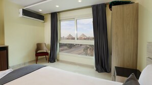 A hotel room with a large bed, a chair, a desk, and a view of pyramids. - Brothers Pyramids View (Giza)