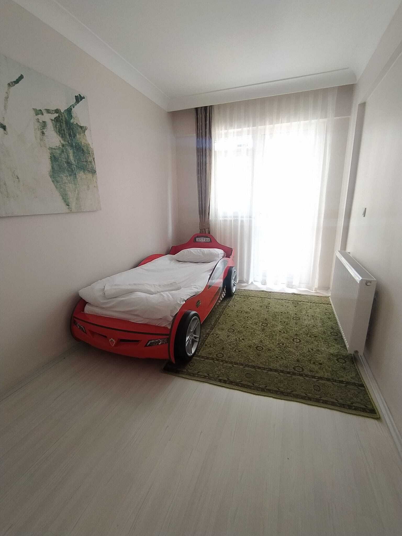 A bedroom with a bed, a radiator, a window with curtains, and a painting on the wall.