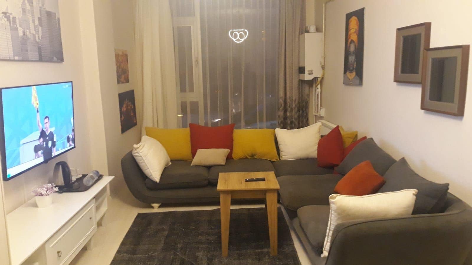 A living room with a sectional sofa, a coffee table, a flat-screen TV, and a window with curtains.
