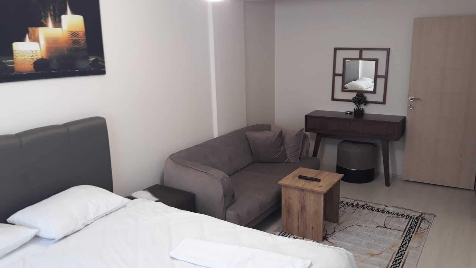 Habitación de hotel con cama, sofá, una pequeña mesa de madera, escritorio, espejo y puerta.