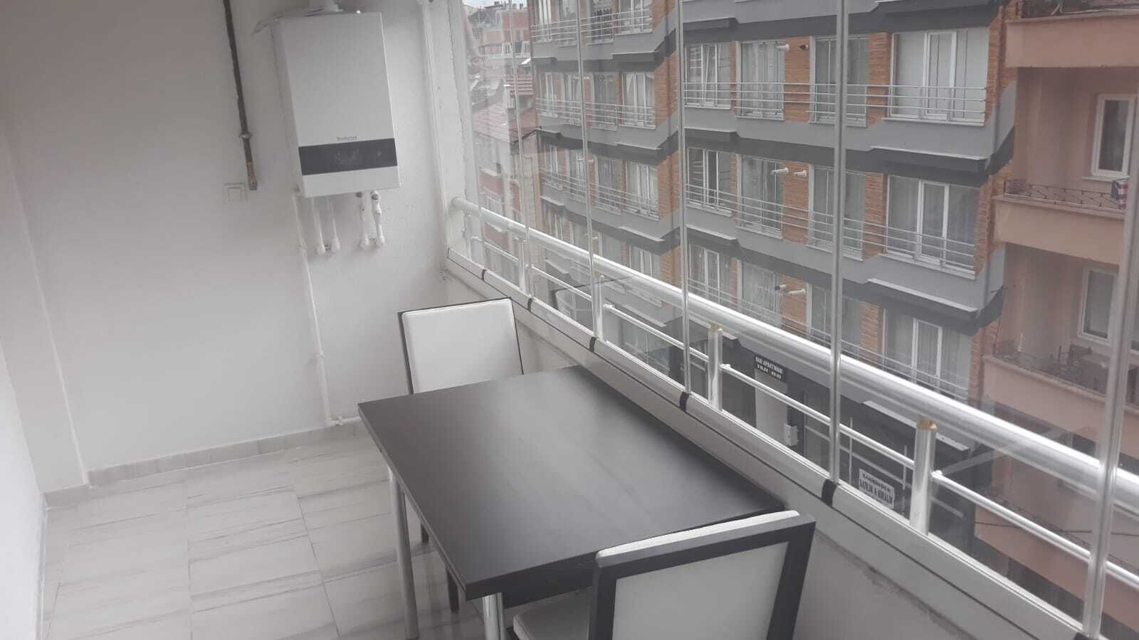Een balkon met een tafel en stoelen, uitzicht op een woongebouw en een boiler aan de muur.