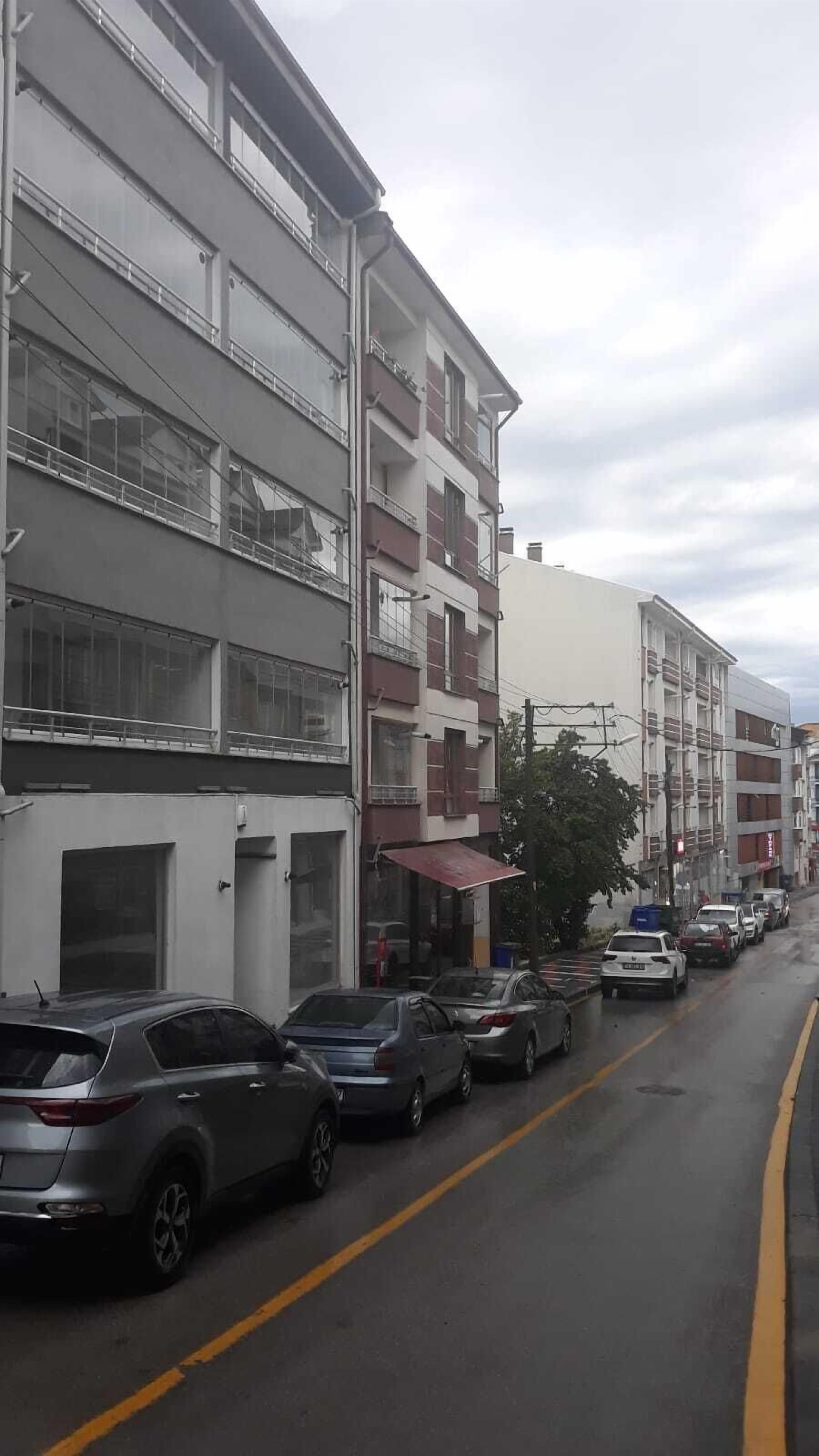 Palazzi residenziali a più piani con balconi, auto parcheggiate e strada bagnata.