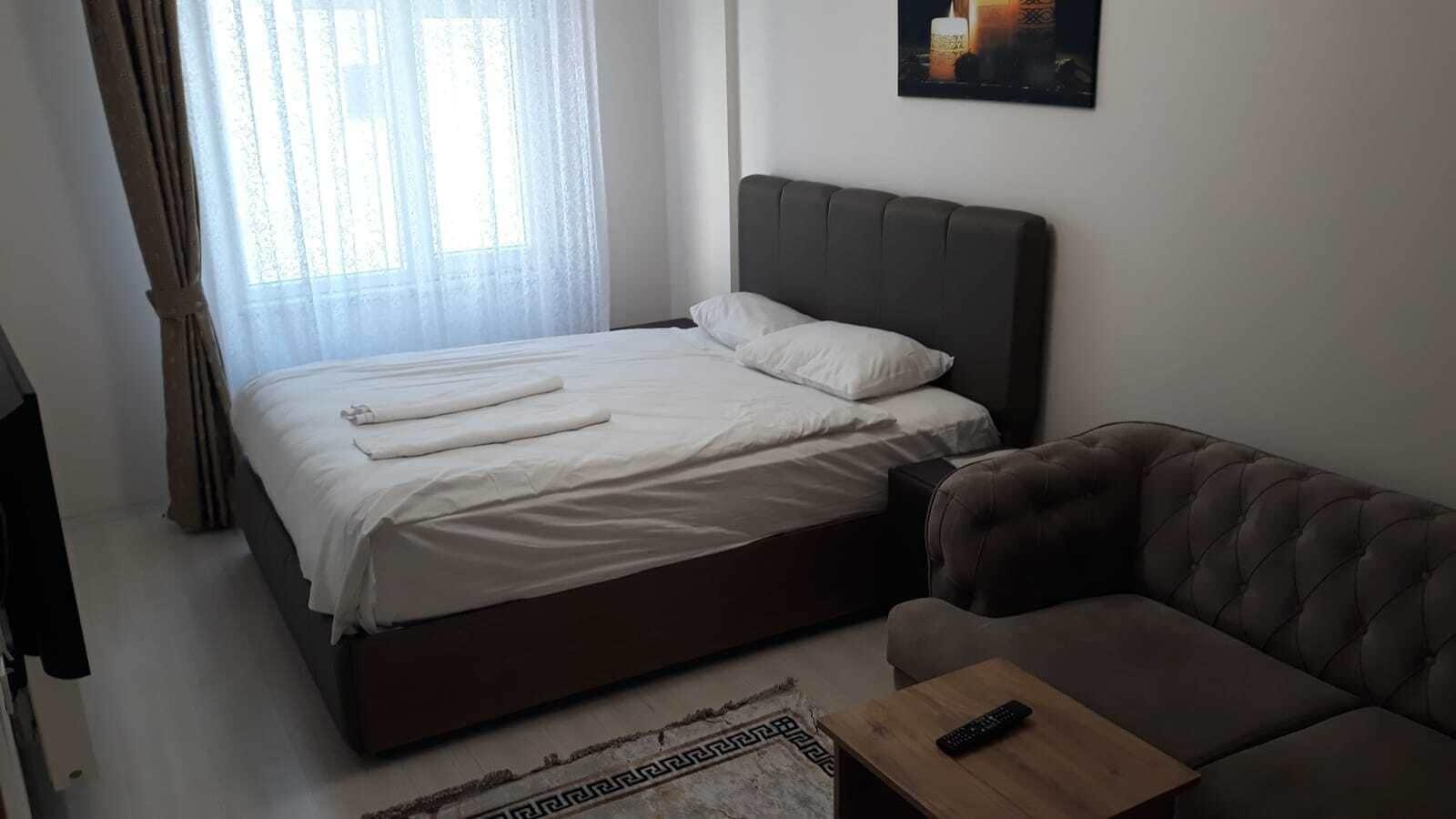 A bedroom with a bed, a sofa, a remote control on a side table, and a painting on the wall.