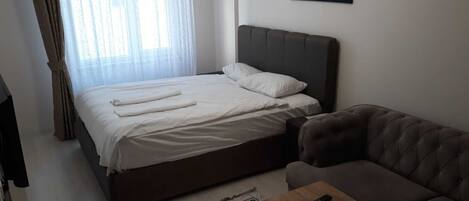 A bedroom with a bed, a sofa, a remote control on a side table, and a painting on the wall.