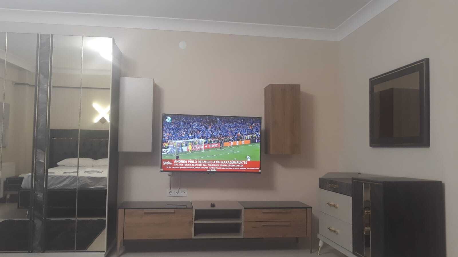 A hotel room with a bed, a TV mounted on the wall, a wooden cabinet, and a mirror.
