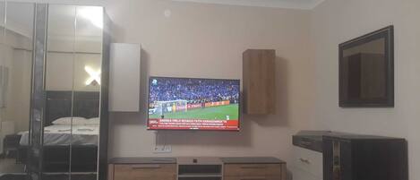 A hotel room with a bed, a TV mounted on the wall, a wooden cabinet, and a mirror.