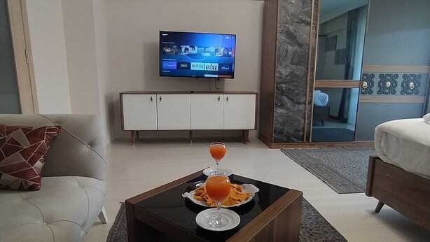 Un saló modern amb televisió de pantalla plana, un sofà, una taula baixa amb aperitius i un armari amb mirall.