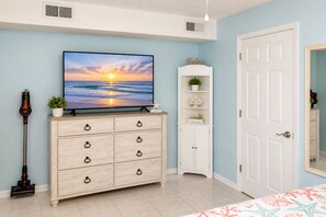 Une pièce avec un téléviseur diffusant une image de coucher de soleil, une commode en bois, une armoire blanche et une porte.
