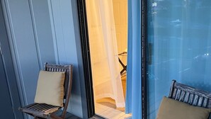 A wooden deck with two wooden chairs, a glass door with a white curtain, and a view of the sky and power lines.