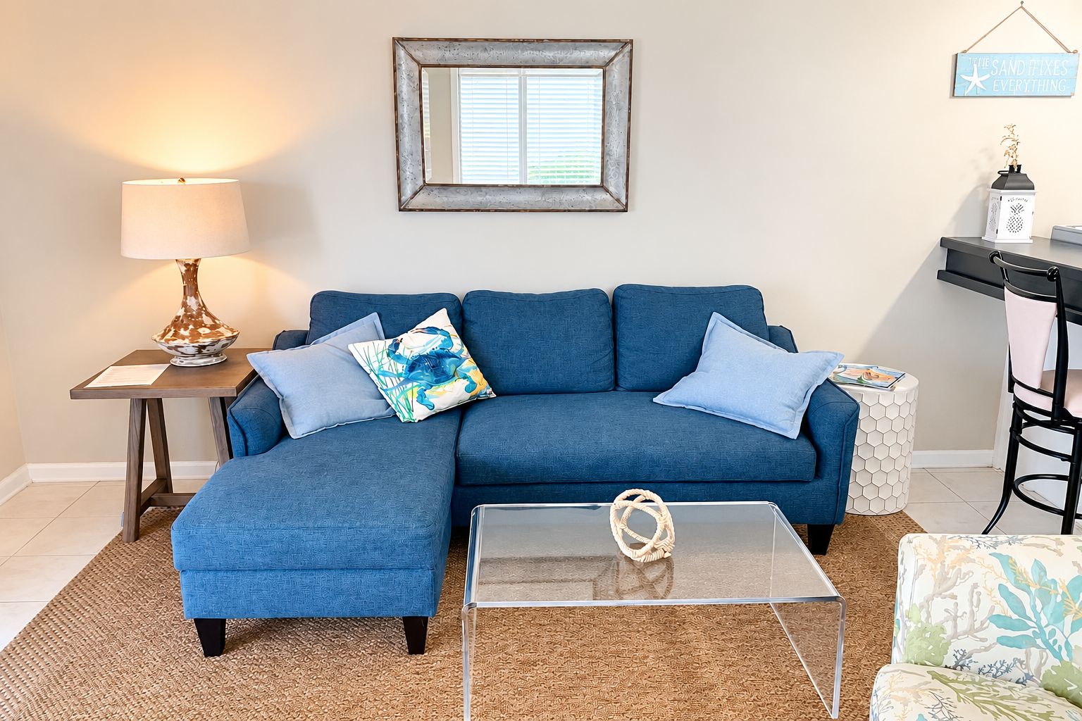 Ein Wohnzimmer mit einem blauen Sofa, einem Glastisch, einer Lampe und einem gerahmten Bild an der Wand.