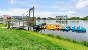 A lakeside dock with paddle boats, a wooden bridge, and buildings in the background.