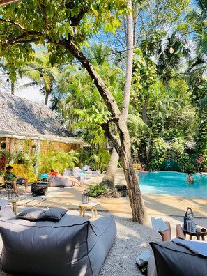 A poolside area with lounge chairs, a thatched-roof structure, and lush greenery. - Norte Nosara (Nosara)
