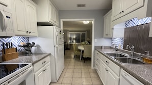 A kitchen with white cabinets, a microwave, and a sink. There is a dining area visible in the background. - Coastal Cottage/The Kindness Cottage (Jekyll Island)