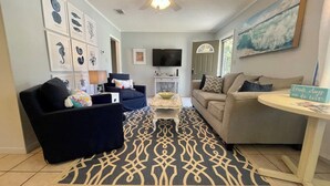A living room with a ceiling fan, a television, and a coffee table. - Coastal Cottage/The Kindness Cottage (Jekyll Island)