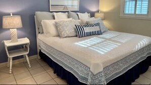 A bedroom with a bed, pillows, a nightstand, a lamp, and a window. - Coastal Cottage/The Kindness Cottage (Jekyll Island)