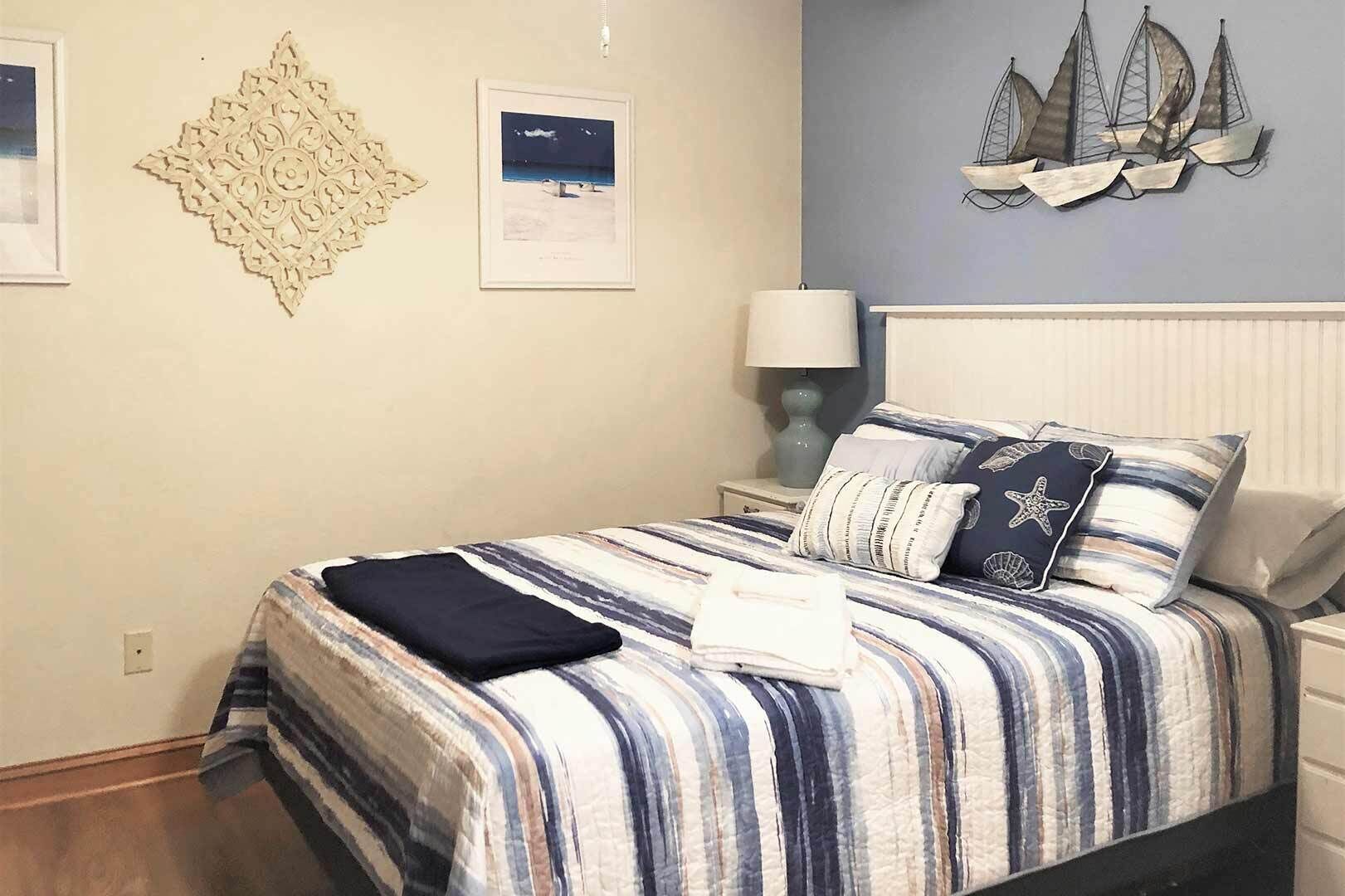 A neatly made bed with striped bedding and starfish pillows, a wall-mounted ship decoration, and a framed picture of a beach scene.