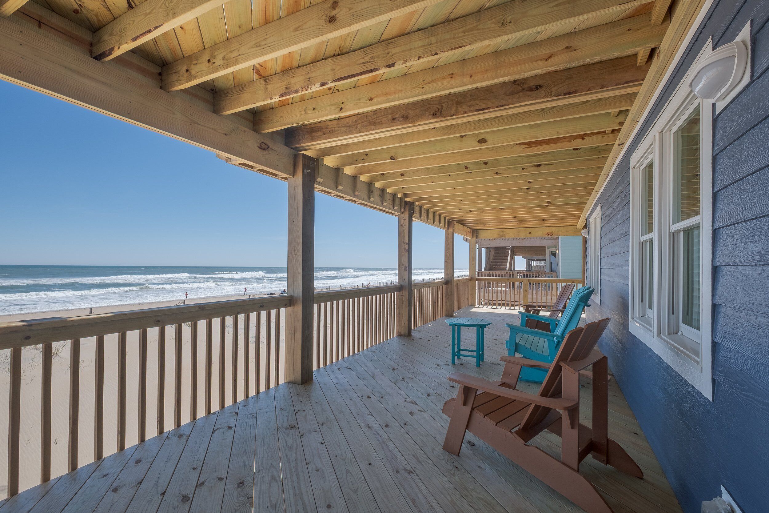 A wooden deck with a view of the ocean, wooden chairs, and a small table.