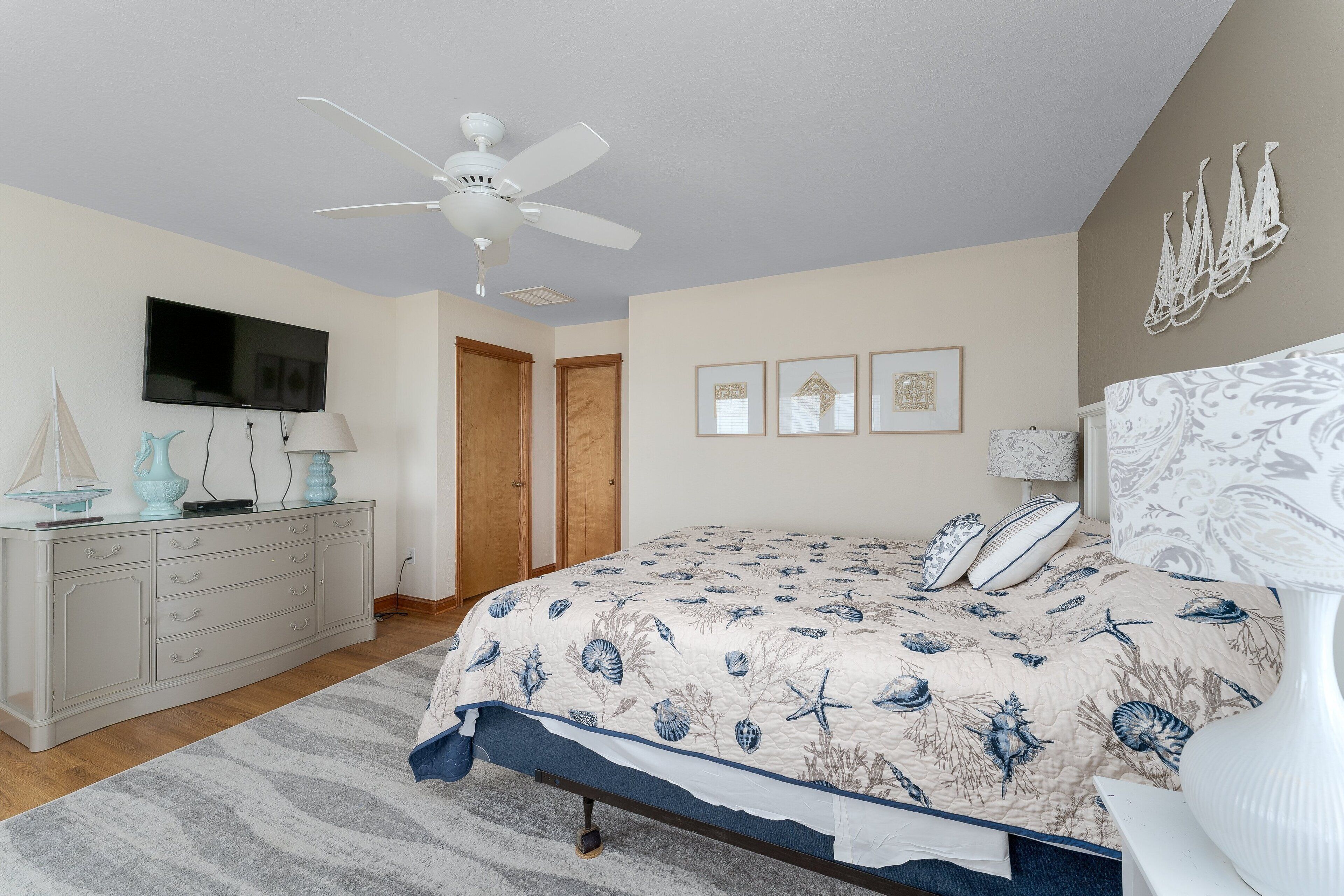 Ein Schlafzimmer mit einem Bett, einem Deckenventilator, einem Schminktisch, einem Fernseher und gerahmten Bildern an der Wand.