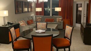 A modern living room with a round dining table, orange chairs, a sofa, and a chandelier.