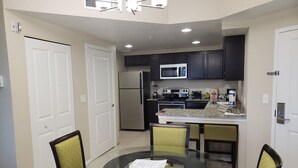 A compact kitchen with dark cabinets, a microwave, and a refrigerator. There is a dining table with chairs in the foreground.