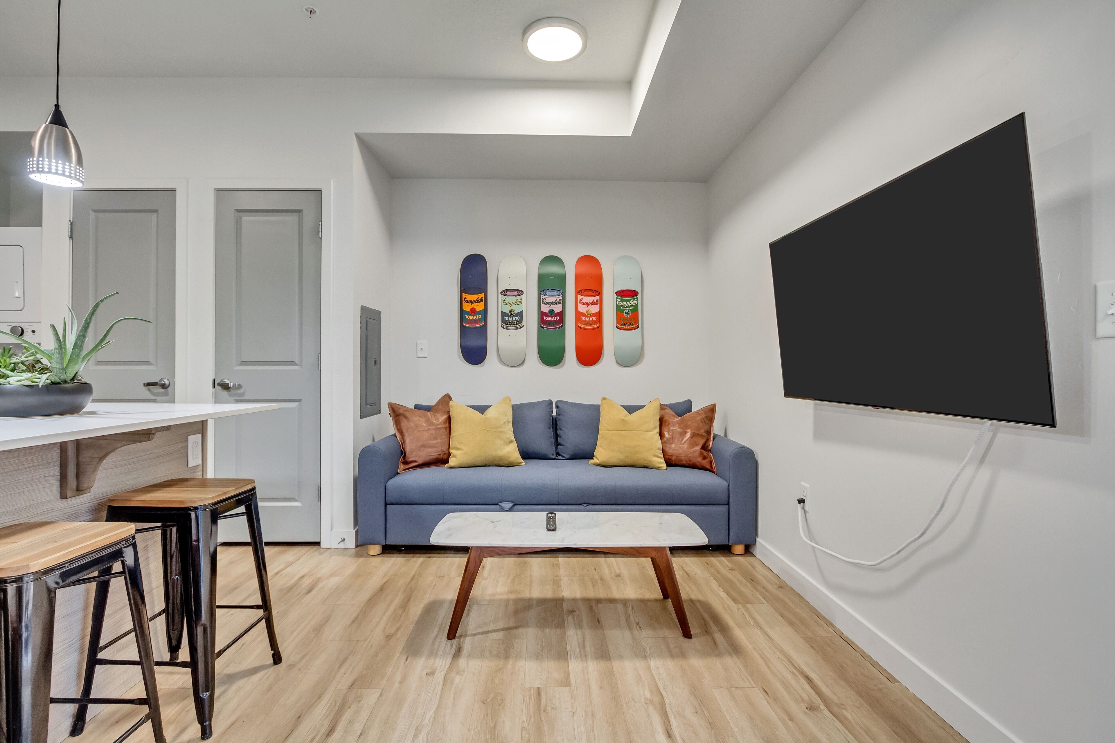 A modern living room with a blue sofa, wooden coffee table, and skateboard art on the wall.