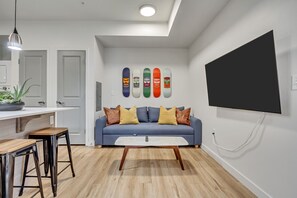 Un salon moderne avec un canapé bleu, une table basse en bois et une œuvre d’art sur le thème du skateboard accrochée au mur.