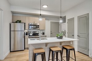 Une cuisine moderne dotée d’appareils électroménagers en acier inoxydable, de tabourets de bar en bois et de luminaires suspendus.