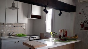 A kitchen with white cabinets, a built-in stove, a window, and a countertop with fruits and utensils. - Cozy villa in the heart of the Luberon (Apt)