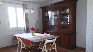 A dining area with a table set for four, white chairs, a wooden cabinet with glass doors, and a window with curtains. - Cozy villa in the heart of the Luberon (Apt)