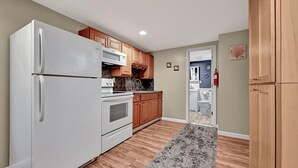 A modern kitchen with white appliances, wooden cabinets, and a grey rug. - Cozy Coastal Cottage 2 Steps From The Beach, Beach Badges, Linens & Towels (Seaside Heights)