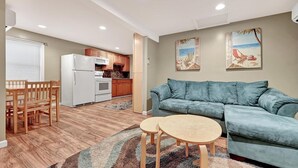 A compact living space with a kitchenette, a blue sofa, a dining table with chairs, and two wall-mounted paintings. - Cozy Coastal Cottage 2 Steps From The Beach, Beach Badges, Linens & Towels (Seaside Heights)