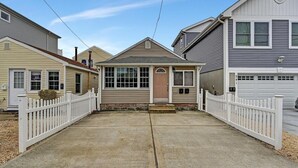 A residential street with houses, a driveway, and a white picket fence. - Cozy Coastal Cottage 2 Steps From The Beach, Beach Badges, Linens & Towels (Seaside Heights)
