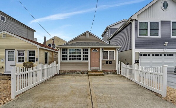 A residential street with houses, a driveway, and a white picket fence.