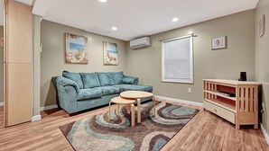 A living room with a blue sofa, a small round table, a wooden cabinet, and a patterned rug. - Cozy Coastal Cottage 2 Steps From The Beach, Beach Badges, Linens & Towels (Seaside Heights)